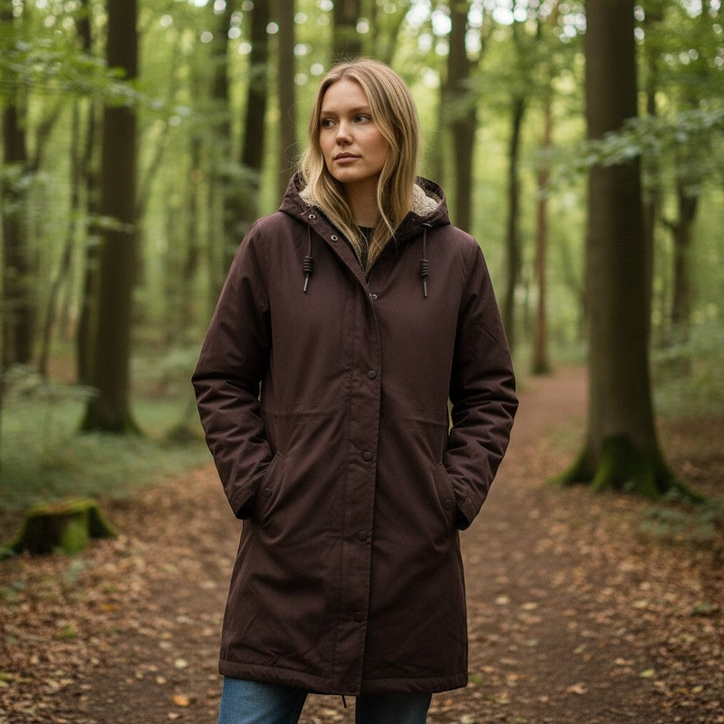Woman wearing a brown Get The High Street Seasalt Plant Hunter waterproof coat with a hood in a forest setting